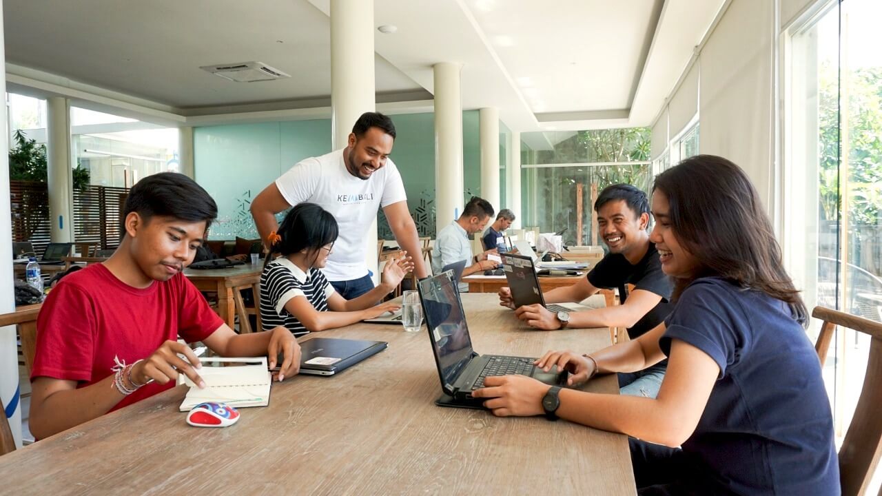 Terdapat beberapa orang yang duduk dan melakukan aktivitas seperti membaca buku dan bekerja di depan laptop